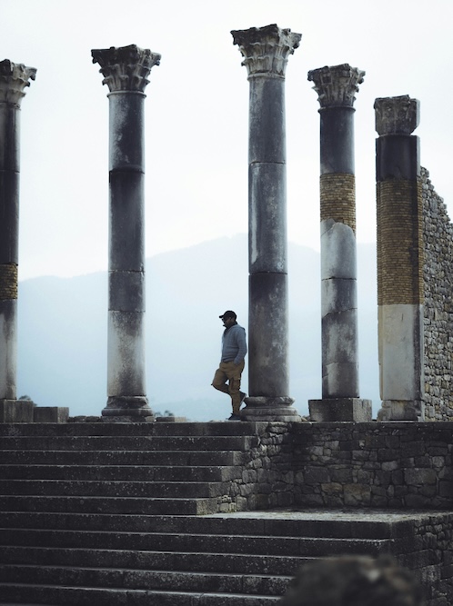 Les colonnes romaines de Volubilis se dressent dans un ciel brumeux. Un homme tout petit au pied des colonnes magistrales.